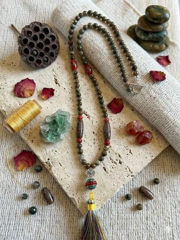 A mala necklace with beads, crystals, petals, and stacked stones on a textured fabric.
