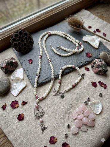 Delicate beaded jewelry with natural stones and floral motifs on a rustic fabric and slate background.