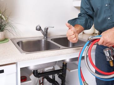 Plumber giving thumbs up near kitchen sink with tools.