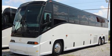 White coach bus parked on gravel under a blue sky.