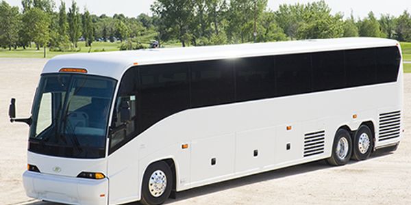 A large white tour bus parked on a paved surface with greenery in the background.