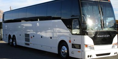 White luxury motorcoach bus parked outdoors under clear sky.