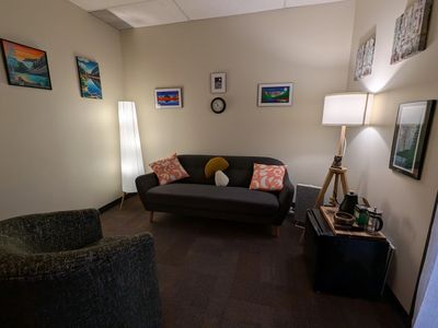 Therapy office with a chair, couch and art on the wall. 