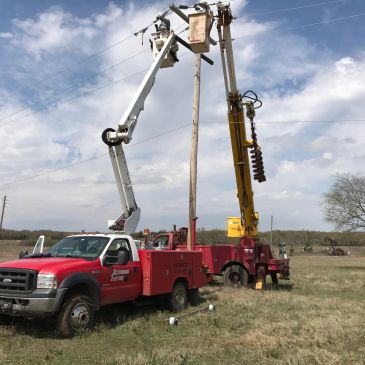 Utility workers fixing power lines with bucket trucks in a field.