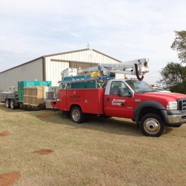 Red utility truck with equipment parked outside a large shed.