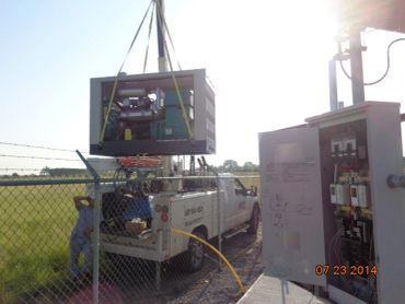 Crane lifting equipment near a utility truck in a fenced area.