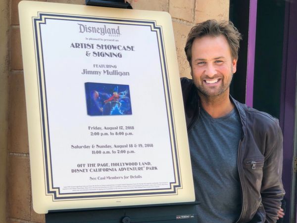 Man smiling next to Disneyland event sign.