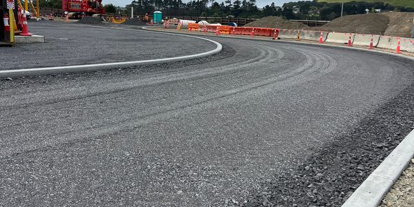 Curved asphalt road under construction with construction barriers.
