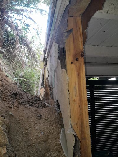 Wall collapse caused by soil erosion leaning against a structure.