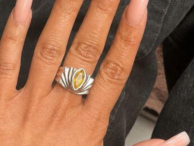 Hand with a silver ring featuring a yellow gemstone.