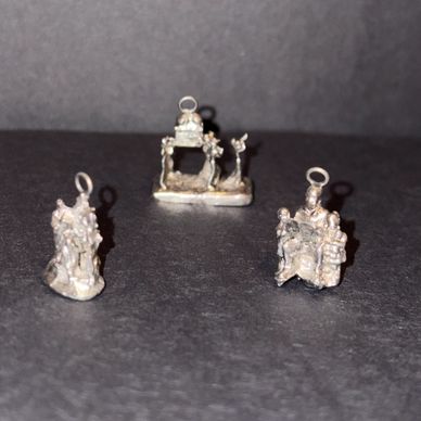 Three small, detailed silver charms on a dark surface.