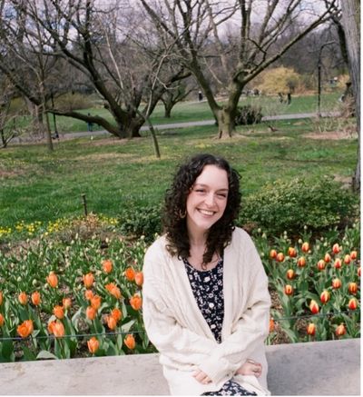 A smiling woman sitting near a bed of orange tulips in a park.