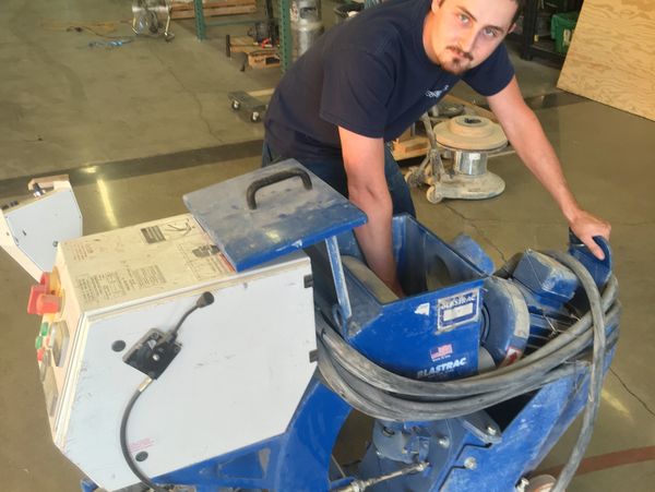 Man operating a large blue industrial floor machine indoors.