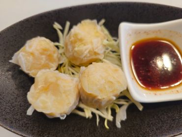 Four shumai dumplings with dipping sauce on a black plate.