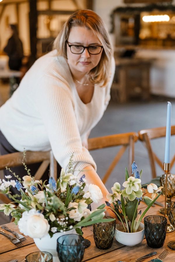 Woman arranging flowers on a dining table.