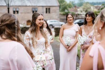 Bride smiling with bridesmaids in blush dresses outdoors.