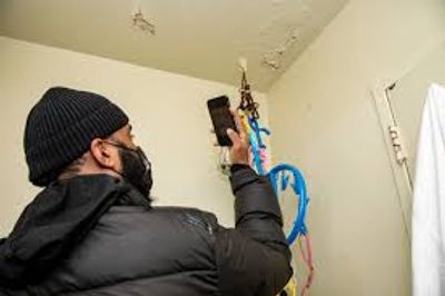 Man inspecting ceiling damage with phone light.