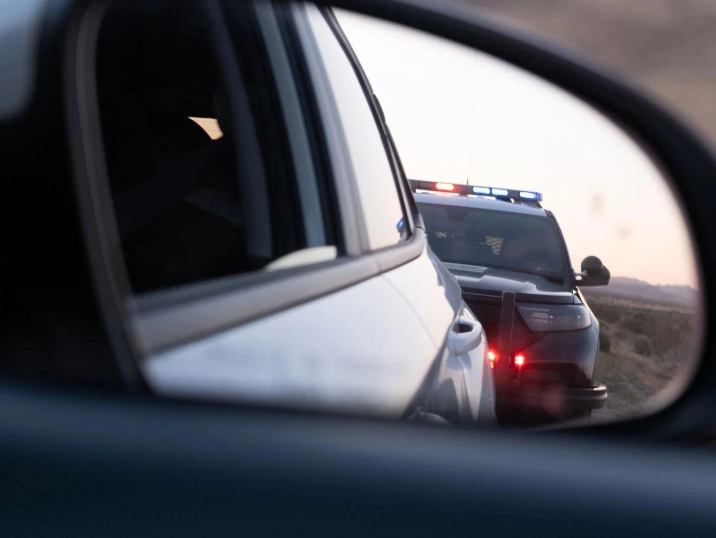 Police car with flashing lights seen in a rearview mirror during a traffic stop.