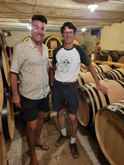 Men smiling in front of wine barrels in France