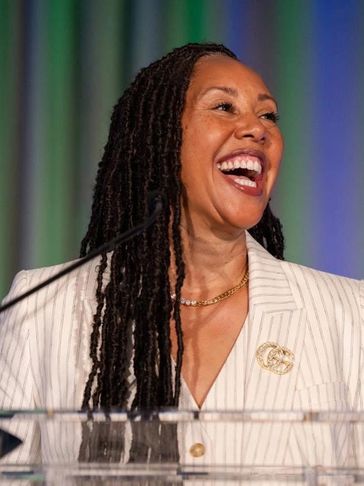 A woman with long dreadlocks laughing behind a podium.