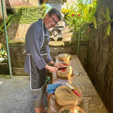 Man cooking outdoors with chopping boards and knives.
