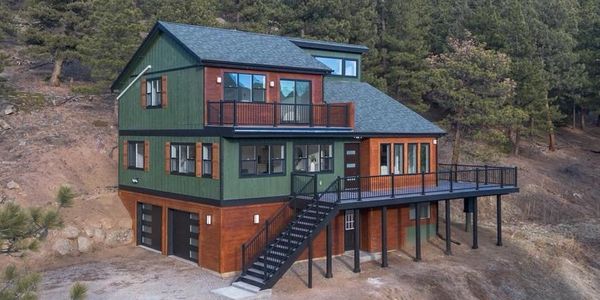 A modern mountain home with green siding, wood accents, and a large wraparound deck.