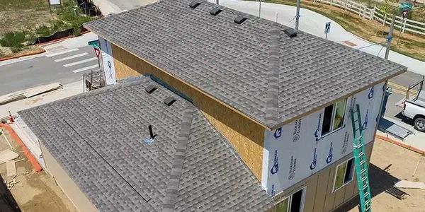 A new residential roof with fresh asphalt shingles is being installed on a modern two-story home.