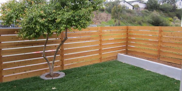 A modern horizontal wood fence encloses a small, neatly landscaped backyard with green grass.
