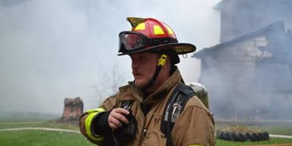 Firefighter in full gear amidst smoke from a fire scene.