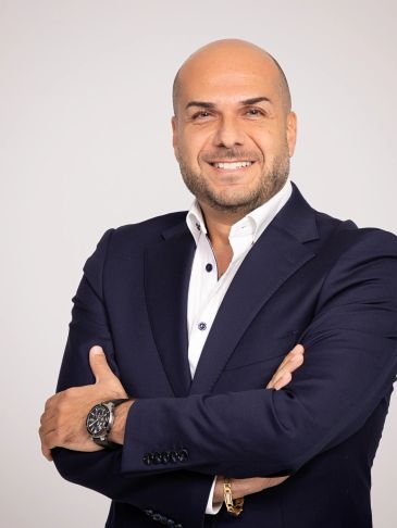Smiling bald man in a navy suit with arms crossed.