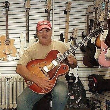 Man smiling while holding an electric guitar in a music store.
