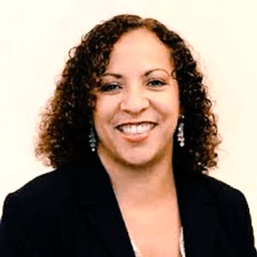 Smiling woman with curly hair wearing a black blazer and earrings.