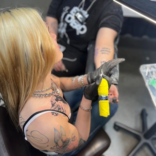 Tattoo artist working on a client's arm in a studio.