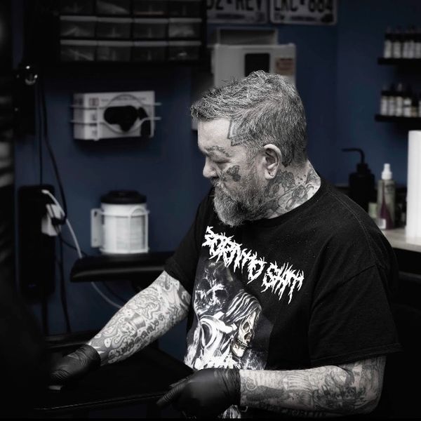 Tattoo artist wearing black gloves and a graphic tee, focused on work.