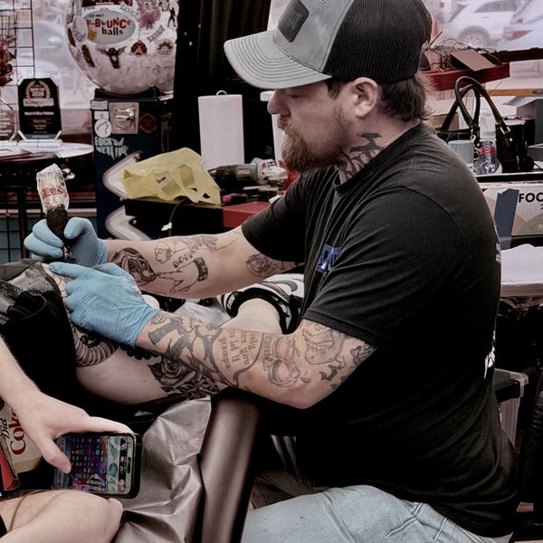 Tattoo artist in gloves working on a client's leg tattoo.