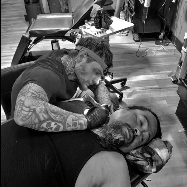 Tattoo artist inks a man's neck in a tattoo studio.