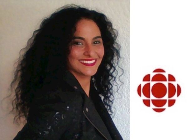 A smiling woman with curly hair posing beside a red logo on a white wall.
