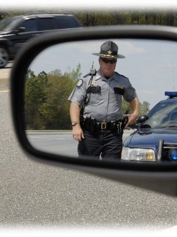 Police officer approaching car, seen through side mirror.
