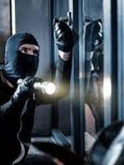 Masked burglar using flashlight to break into a building at night.