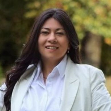 Smiling woman with long dark hair wearing white blazer outdoors.