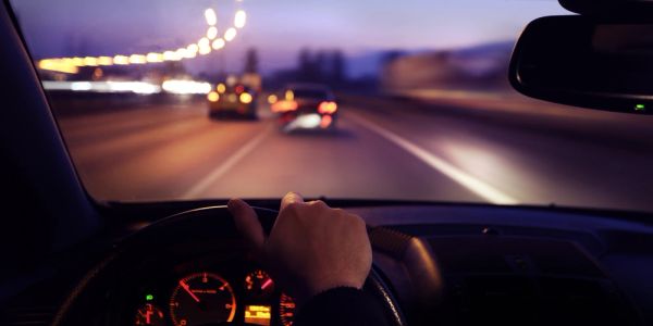 Driver's hand on steering wheel during night drive on highway.