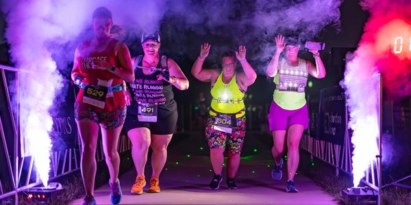 Four women running a night race with colorful smoke effects and bright lights.