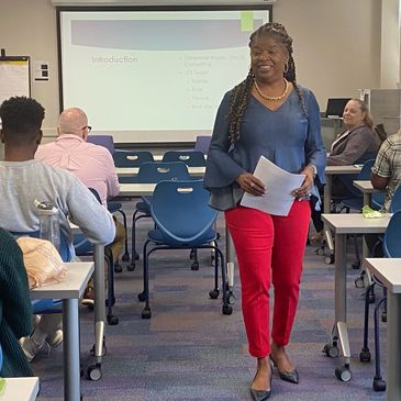 A woman confidently leads a classroom session in front of engaged students.
