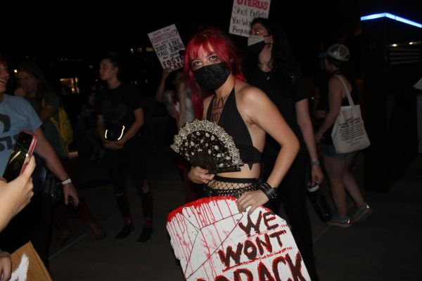 Protester with red hair holding a fan and sign at night.