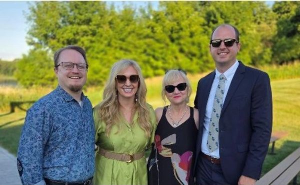 Group of four people smiling outdoors in sunglasses.