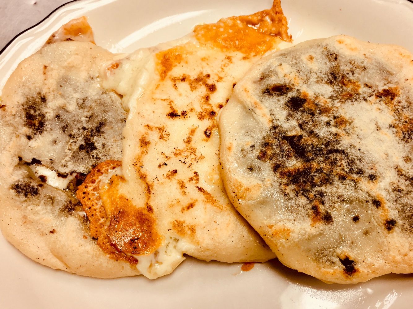 Three round, overlapping pupusas on a plate. The middle pupusa has crispy cheese edges.