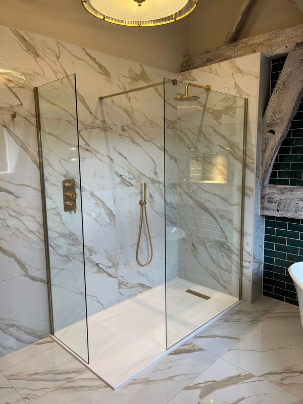 Modern walk-in shower with glass panels and marble walls.