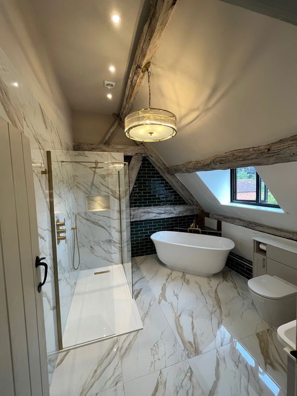 Modern attic bathroom with marble tiles, freestanding tub, and rustic wooden beams.