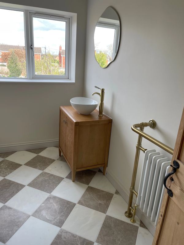 Minimalist bathroom corner with wooden vanity and round mirror.