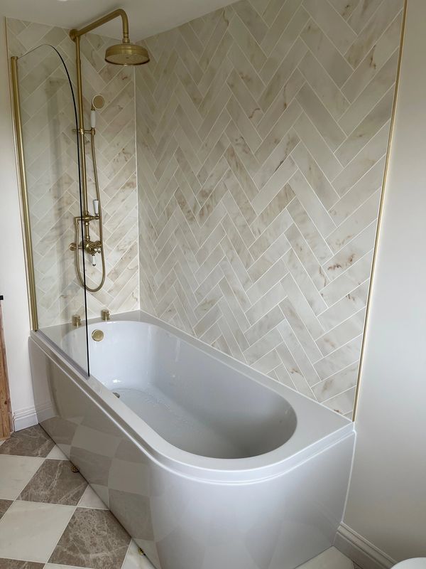Modern bathtub with gold shower fixtures and tiled wall.